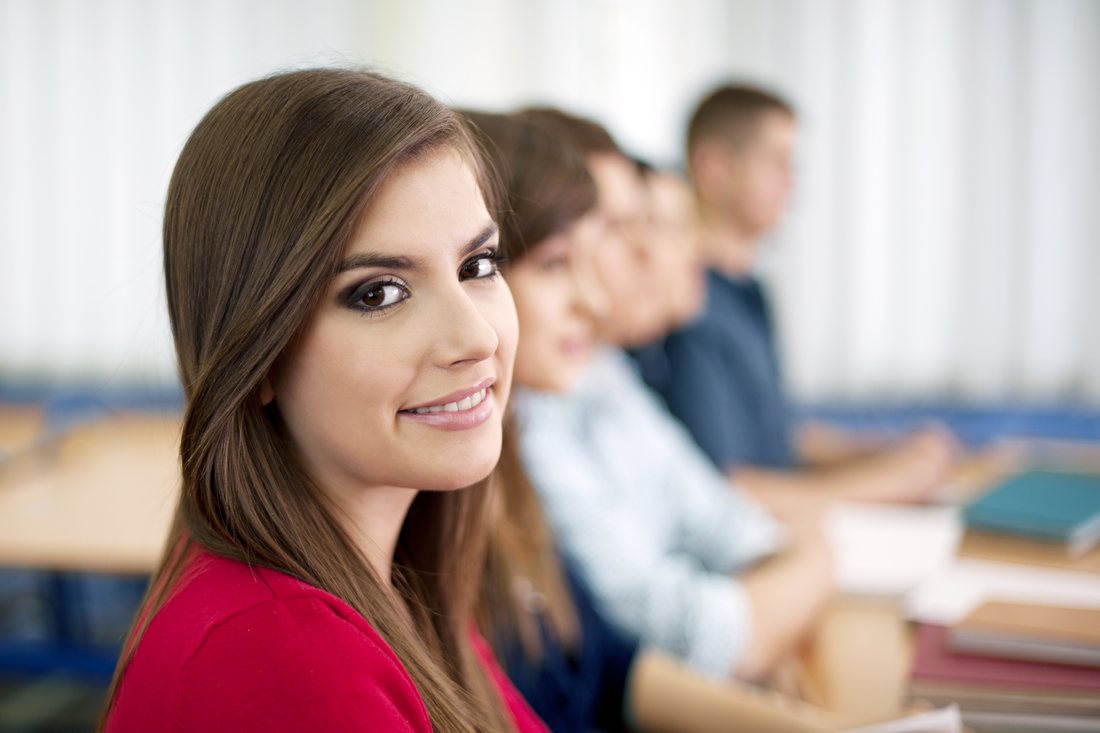 Uśmiechnięta studentka na zajęciach w sali, w tle grupa przy ławkach