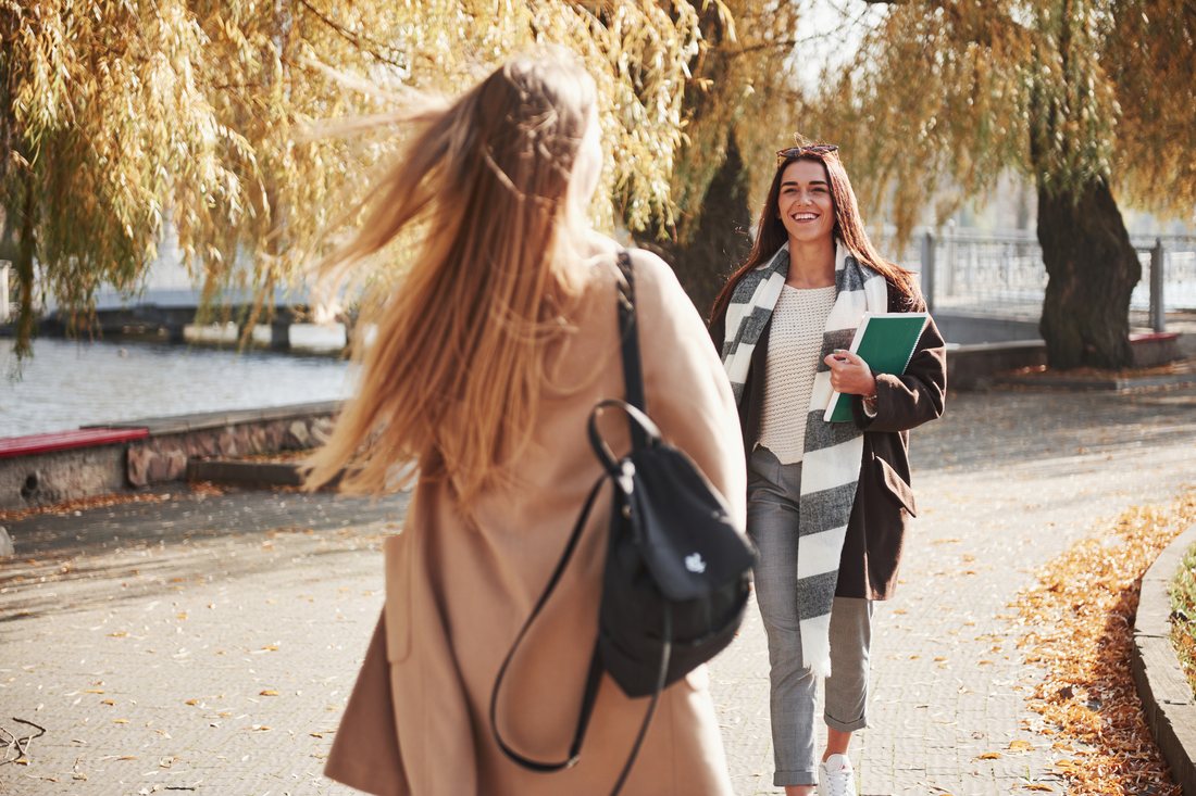Dwie studentki z plecakiem i notesem spotykają się w parku jesienią